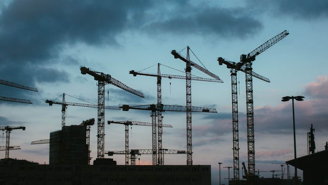 Varias grúas de obra recortadas contra el cielo del atardecer