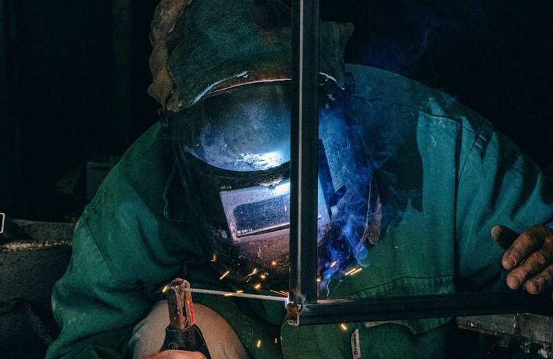 Soldador con máscara y equipo de protección trabajando sobre una pieza metálica