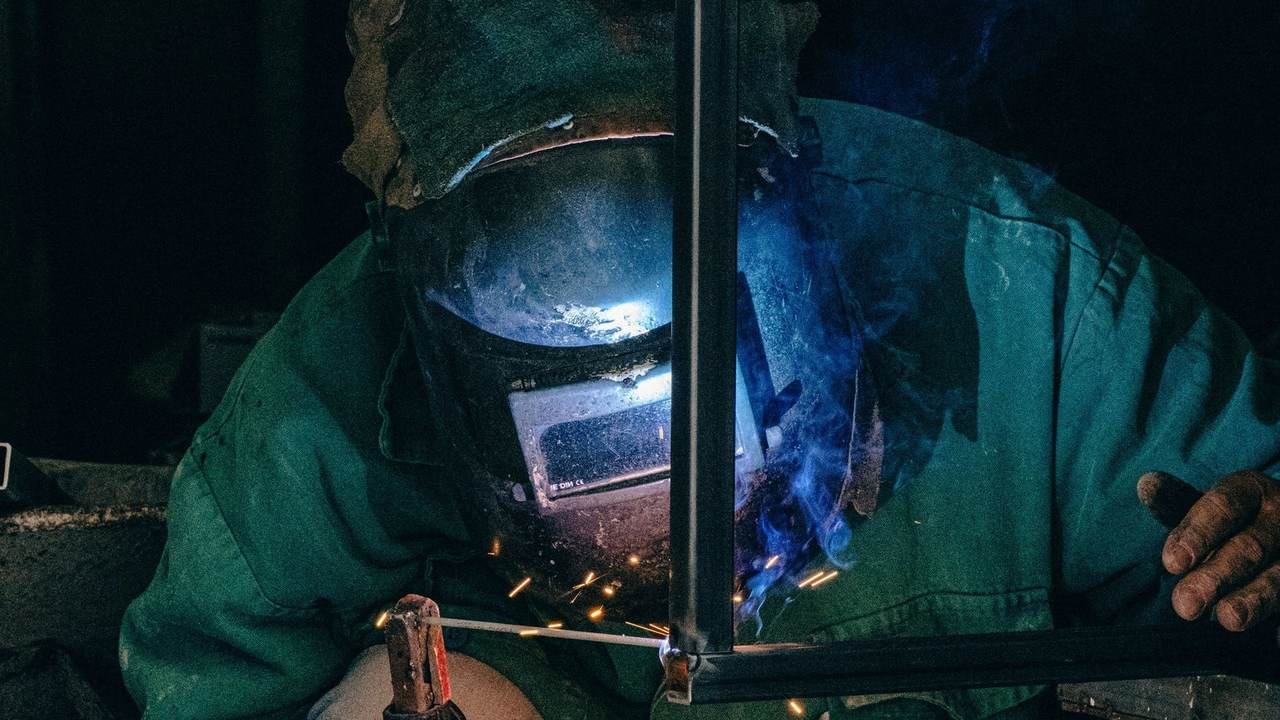 Soldador con máscara y equipo de protección trabajando sobre una pieza metálica