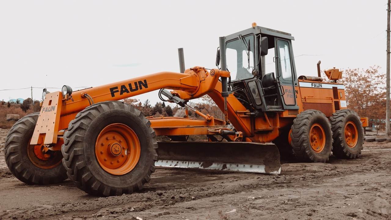 Motoniveladora naranja trabajando en una obra embarrada