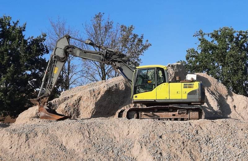 Excavadora amarilla trabajando sobre un montículo de grava en una obra