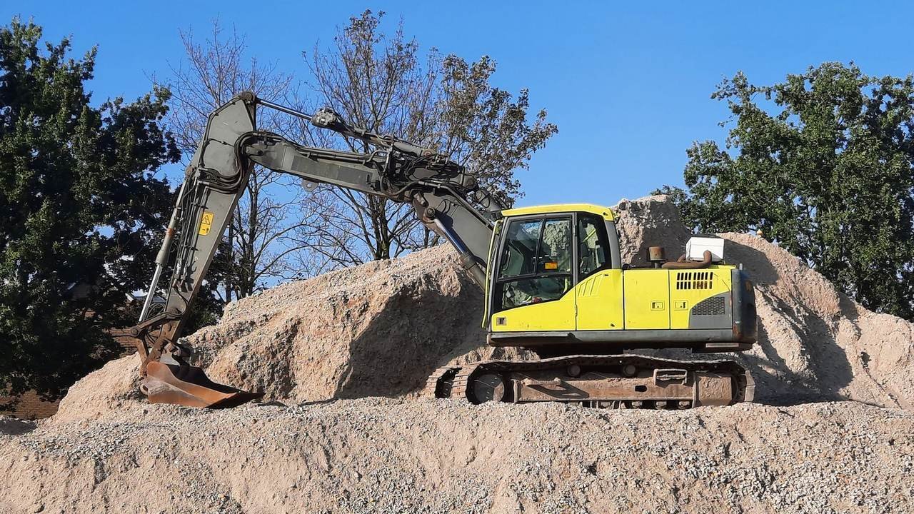 Excavadora amarilla trabajando sobre un montículo de grava en una obra