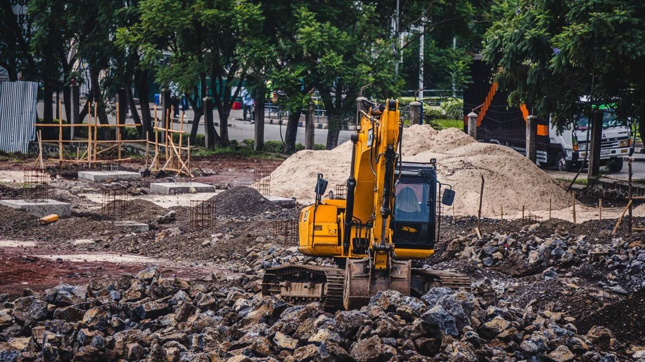 Excavadora amarilla trabajando en una obra urbana entre rocas y árboles