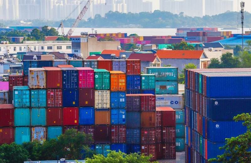 Contenedores apilados de colores en un puerto, con la ciudad al fondo