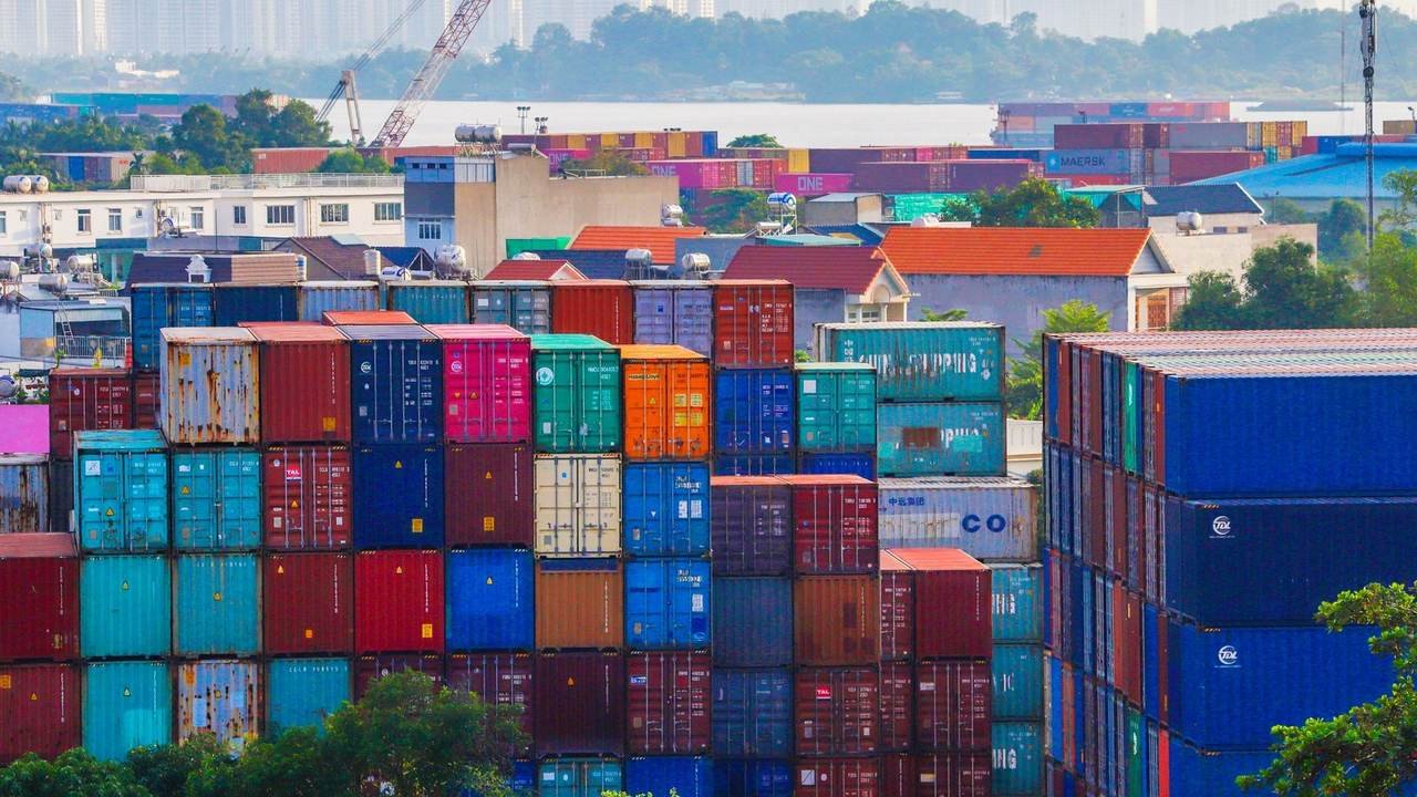 Contenedores apilados de colores en un puerto, con la ciudad al fondo