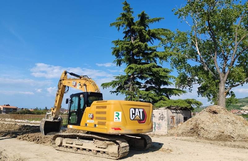 Excavadora Caterpillar trabajando en una obra, con árboles y cielo despejado