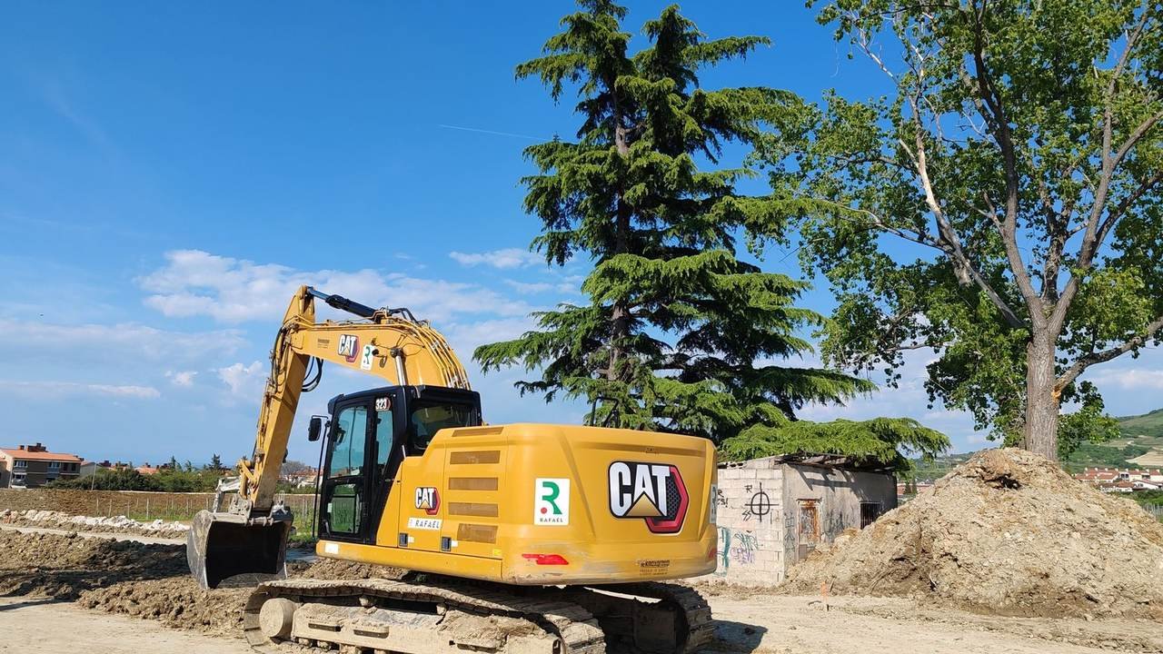 Excavadora Caterpillar trabajando en una obra, con árboles y cielo despejado